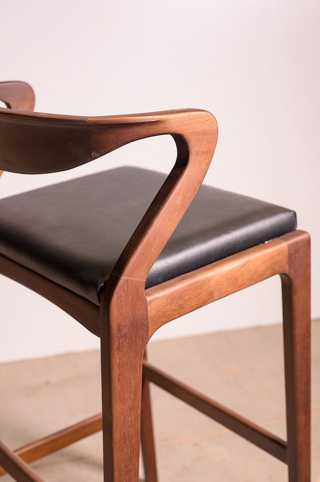 Detalle de taburete de madera con brazo curvo y asiento tapizado en negro